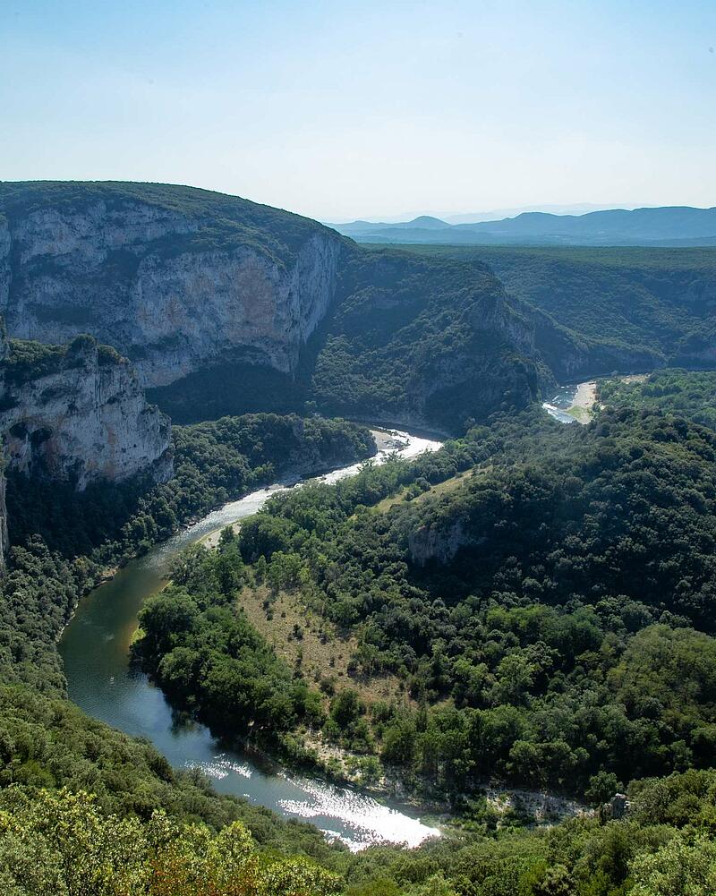 [Translate to Néerlandais:] Panoramic high angle view of the green Ardeche river canyon winding through deep forests and massive stone cliffs near Les Castels campsites.