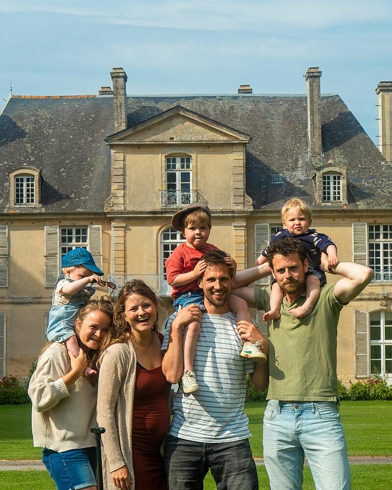 [Translate to Néerlandais:] A joyful group photo of adults and young children smiling together in front of a historic French chateau at a luxury Les Castels holiday estate.